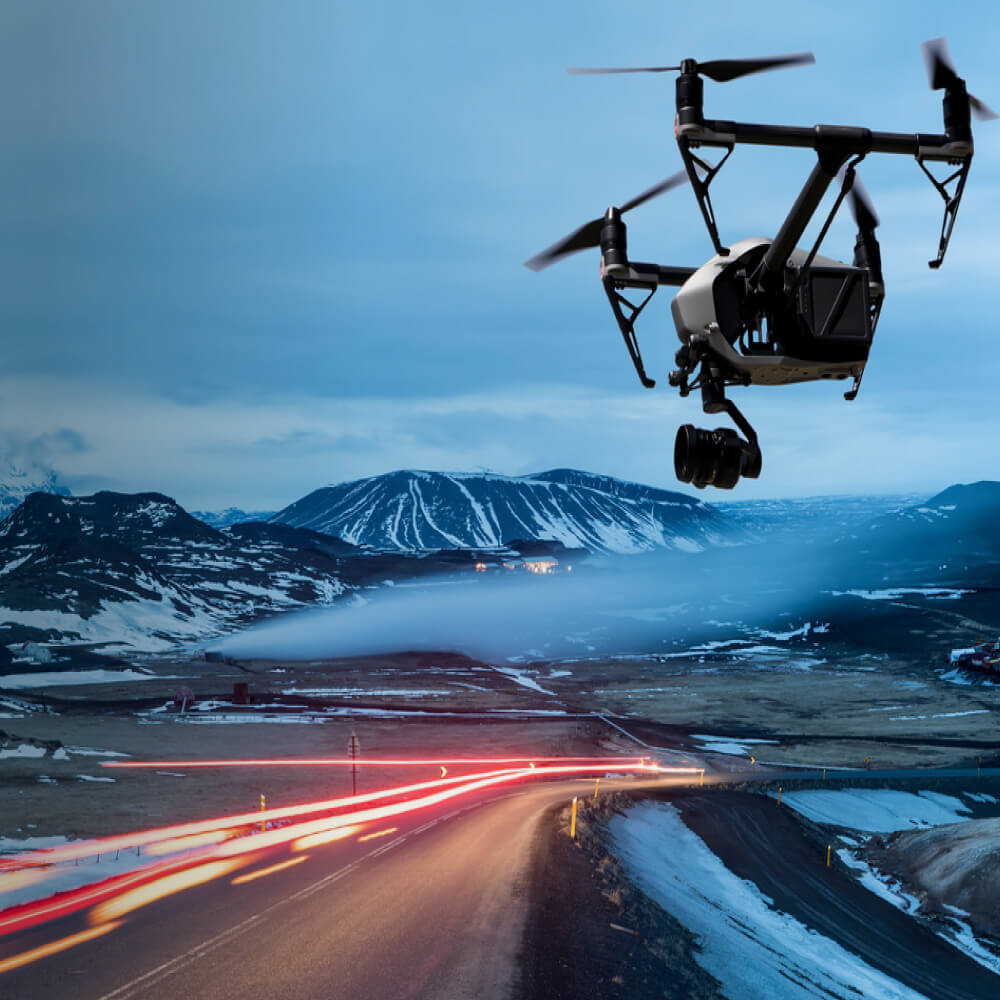 A drone captures an aerial view of a road with majestic mountains in the background